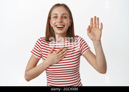 Its me nice to meet you. Smiling friendly blond girl name herself, hold hand on chest and waving, raising arm to make promise, greeting new people Stock Photo