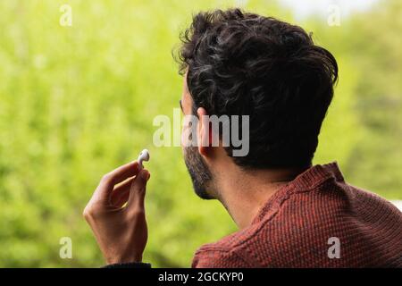 Unrecognizable male with true wireless earphones on background of blurred green grass Stock Photo