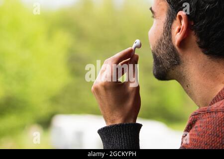 Unrecognizable male with true wireless earphones on background of blurred green grass Stock Photo