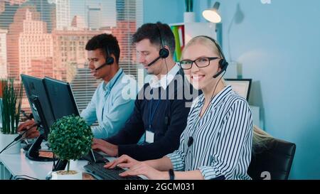 Beautiful female customer service working in busy call center by talking to the international client. Her mixed-race team also taking calls. Stock Photo