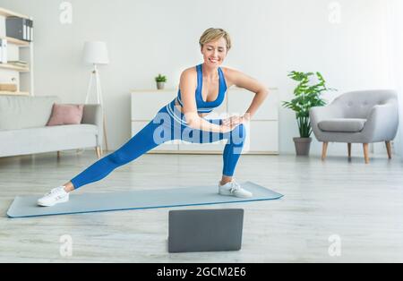 Smiling woman doing side lunges on mat using pc Stock Photo