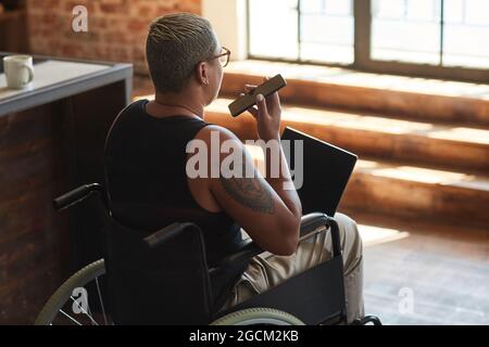 Back view portrait of contemporary tattooed woman with disability using laptop while working from home Stock Photo