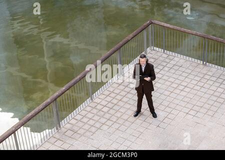 From above of middle aged bearded man in elegant suit browsing on tablet on terrace Stock Photo