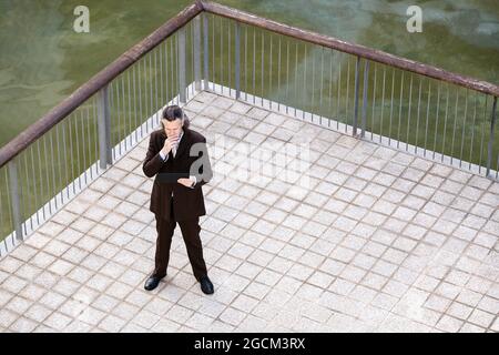 From above of middle aged bearded man in elegant suit browsing on tablet on terrace Stock Photo
