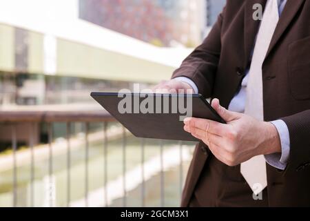 Cropped unrecognizable man in formal outfit browsing tablet while standing on embankment in city Stock Photo