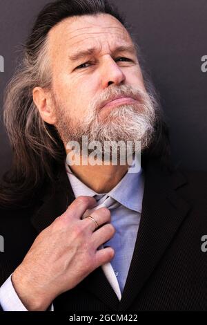 Stressful tired aged gray haired bearded male entrepreneur in formal suit loosening necktie after hardwork Stock Photo