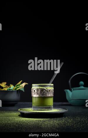 Still life composition with traditional oriental matcha tea served in glass cup with metal ornamental decor on table with ceramic bowls and fresh gree Stock Photo