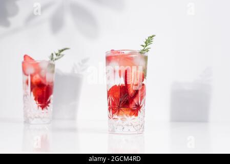 Refreshing summer drink with fresh sliced strawberries and ice cubes with water served in glasses on white table Stock Photo