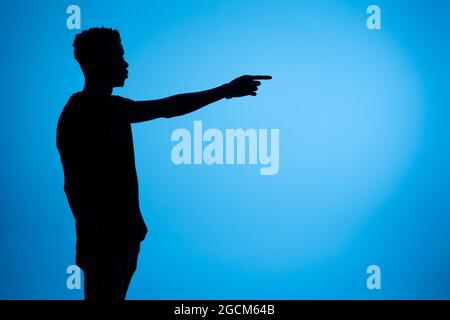 Side view of silhouette of African American male standing with outstretched arm and pointing away on blue background in studio Stock Photo