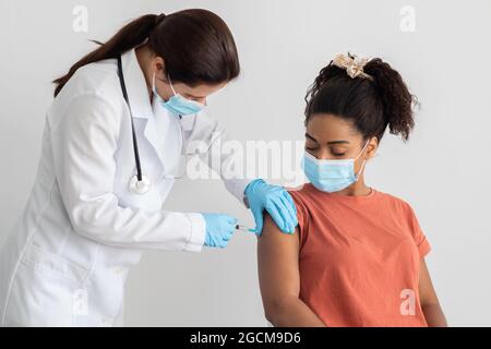 Nurse in white workwear making vaccination for black woman Stock Photo