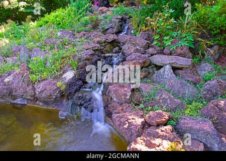 Long exposure shot of a small, man-made waterfall and rock garden in a local park Stock Photo