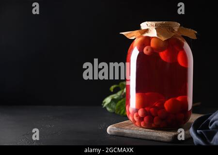 Homemade canned red cherry compote in large glass jar on black background. Space for text. Stock Photo