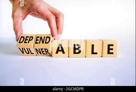 Vulnerable or dependable symbol. Businessman turns wooden cubes and changes the word Vulnerable to Dependable. Beautiful white background, copy space. Stock Photo