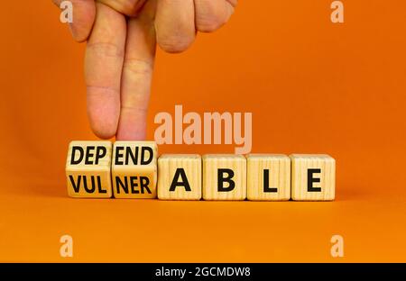 Vulnerable or dependable symbol. Businessman turns wooden cubes and changes the word Vulnerable to Dependable. Beautiful orange background, copy space Stock Photo