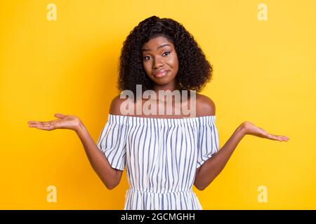 Photo of sweet puzzled dark skin woman wear striped outfit rising arms shrugging shoulders isolated yellow color background Stock Photo