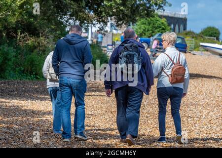 four middle aged friends walking on the beach together on holiday on the isle of wight uk. Friends walking together at the seaside. shingle beach. Stock Photo