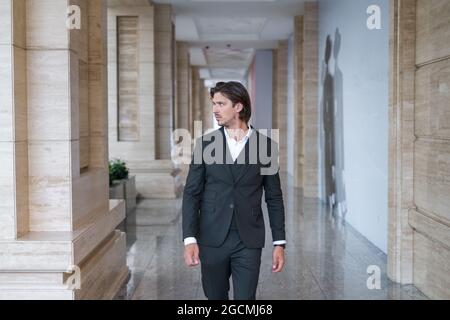 Stylish young brunet man in black suit walking on the street near modern office building. Portrait. High quality photo Stock Photo