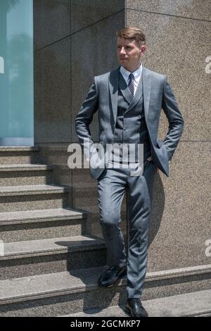Successful businessman in grey formal suit standing on the stairs near office building. High quality photo Stock Photo