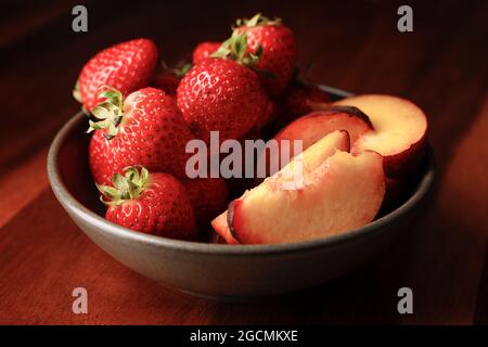 A studio photo of a bowl of fresh strawberries and sliced peaches. Stock Photo