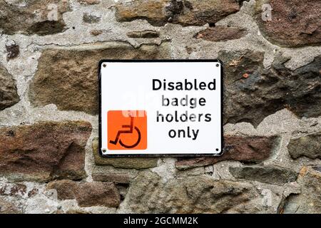 Disabled Badge Holders Only parking sign on a rough stone wall. Stock Photo