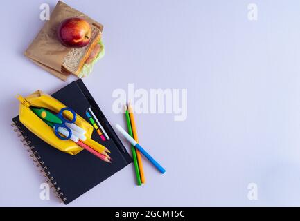 Back to School material. Pencils, notebook and sandwich on purple background. Copy space. Stock Photo