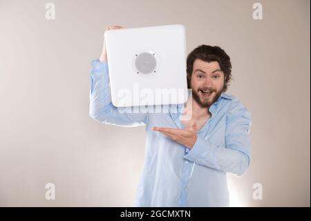 Young attractive man  holding white portable bluetooth speaker on shoulder on gray background Stock Photo