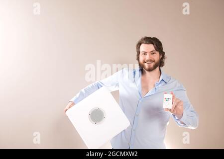 Young attractive man  holding white portable bluetooth speaker and lighting remote control panel on gray background Stock Photo