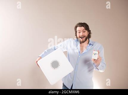 Young attractive man  holding white portable bluetooth speaker and lighting remote control panel on gray background Stock Photo