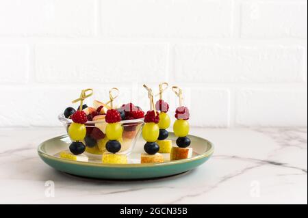 assortment of fruit canapes on a plate against the background of a white brick wall. festive food Stock Photo