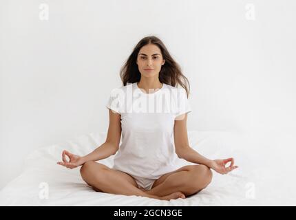 Woman doing yoga exercise on bed at home. Stock Photo