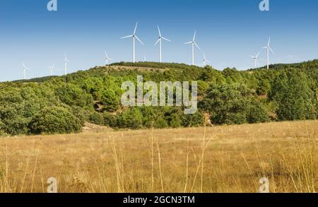 Modern windmills installed on hills in the countryside amidst vegetation. Stock Photo