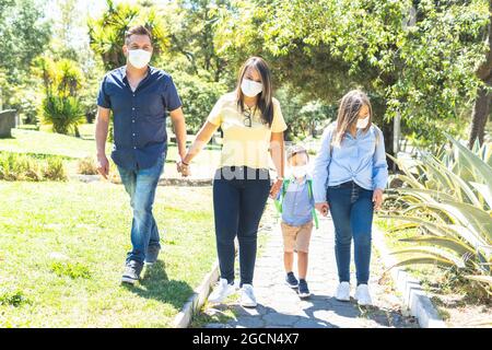Family with face mask walking along a path to drop the children off at school. Back to school Stock Photo