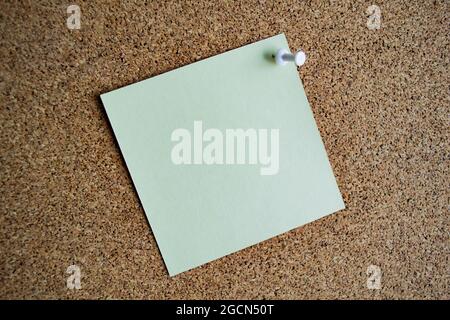 A light green paper note on a cork board, attached with a white pushpin. Copy space. Stock Photo