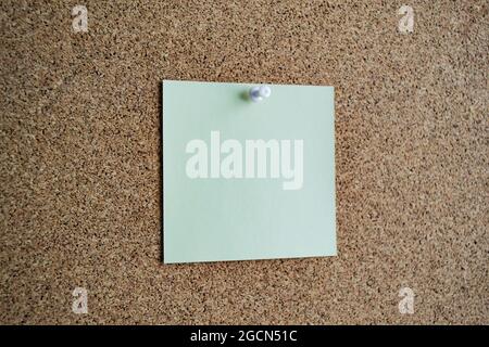 A light green paper note on a cork board, attached with a white pushpin. Copy space. Stock Photo