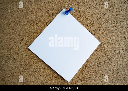 A white paper note on a cork board, attached with a blue pushpin. Copy space. Stock Photo