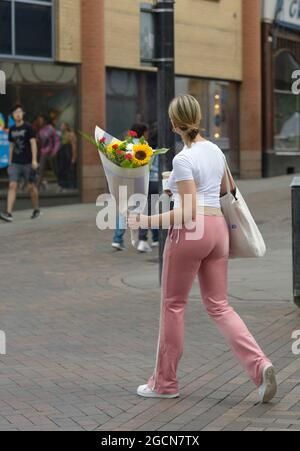 Young woman with flowers, in white top & pink trousers Stock Photo