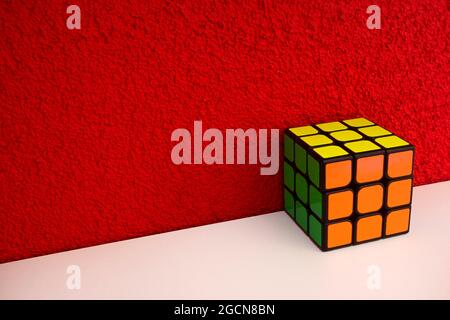 Solved puzzle speed cube on white wooden shelf near red colored wall, colorful rubiks cube with copy space mind challanging Stock Photo