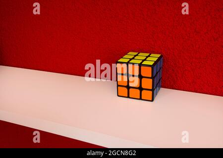 Solved puzzle speed cube on white wooden shelf near red colored wall, colorful rubiks cube with copy space mind challanging Stock Photo
