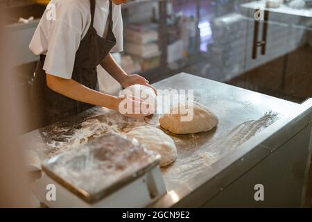 Baker kneads dough for bread at table in craft bakery shop closeup Stock Photo