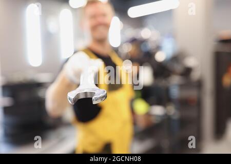 Master mechanic holds out wrench against background of service station Stock Photo