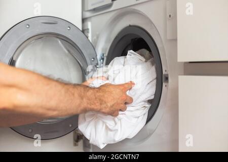 Housework: Man loading white clothes into washing machine Stock Photo
