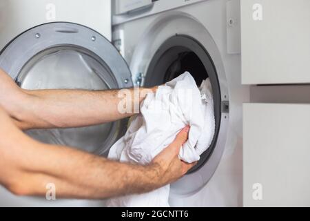 Housework: Man loading white clothes into washing machine Stock Photo