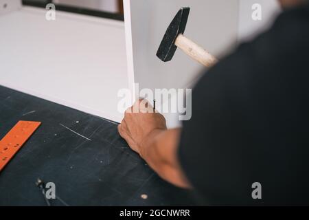 hands nailing a screw with an hammer into a white wooden piece of furniture Stock Photo
