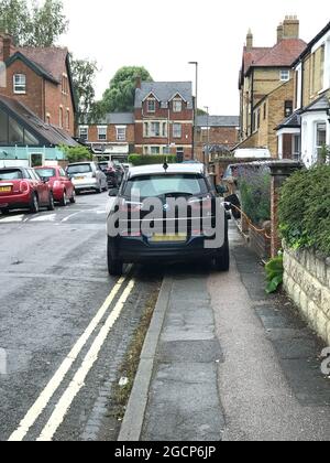 Charging Point ! Charging Infrastructure - charging an electric car with cable hanging across pavement and parked on double yellow lines Stock Photo