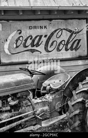 A vinatge tractor parked under a rusted sign for Coca Cola at the Mast General Store in Valle Crucis, North Carolina. Stock Photo