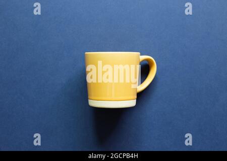 Yellow mug cup on blue background. top view, copy space Stock Photo