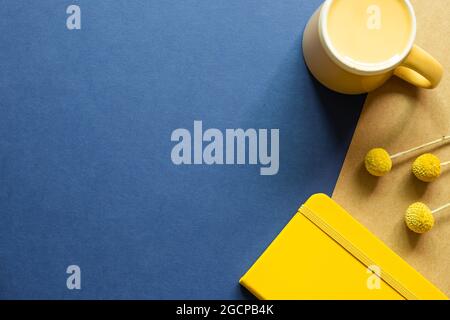Yellow Notebook, mug cup, dry flowers on blue and brown background. flat lay, top view, copy space. Work and study place Stock Photo