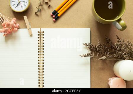 Open notebook with dry flowers, clock, pencils, cup of tea, candles on brown background. top view, copy space Stock Photo