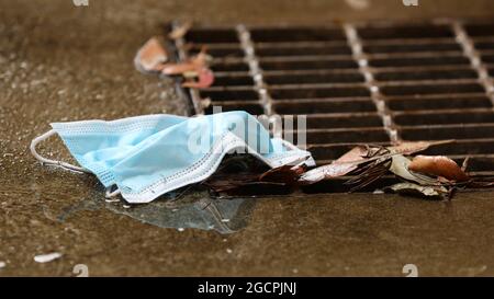 A close up of a discarded used personal protective face mask entering a metal grate on a drain. Growing environmental concern regarding safe disposal Stock Photo