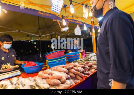 Street food night market at  Putrajaya, near Kuala Lumpur. Salesman with face mask in a seafood street store. the customer is waiting for the fish he Stock Photo